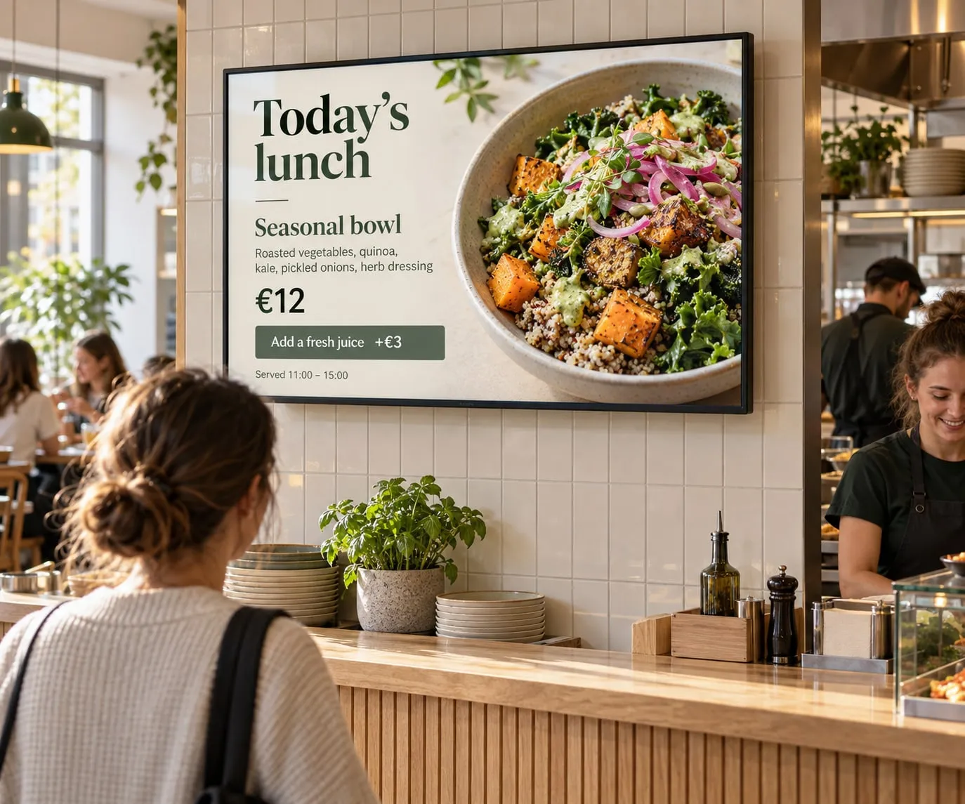 Cliente al bancone di un caffè che guarda uno schermo con il pranzo del giorno: una bowl stagionale a 12 €